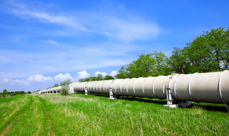 A white oil and gas pipeline running through a field of green grass